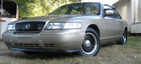 2000 Mercury Grand Marquis - 2000 Mercury Grand Marquis sedan, front 3/4 view, parked on grass with a trailer and house in background.