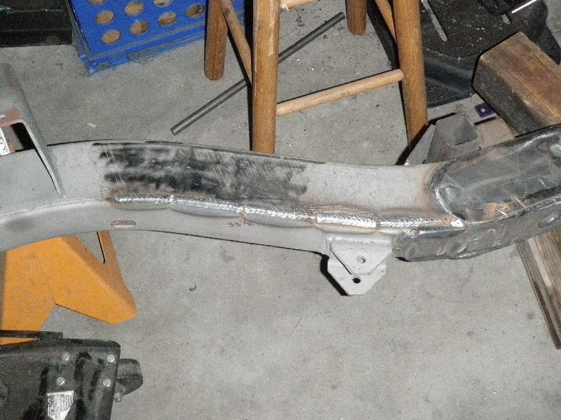 Vehicle frame section with extensive welds and grinding marks, supported by an orange jack stand