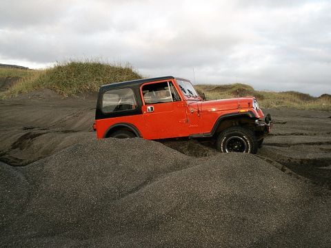 1996 Ford Bronco - An orange Jeep Wrangler navigates through a sandy terrain under a cloudy sky.