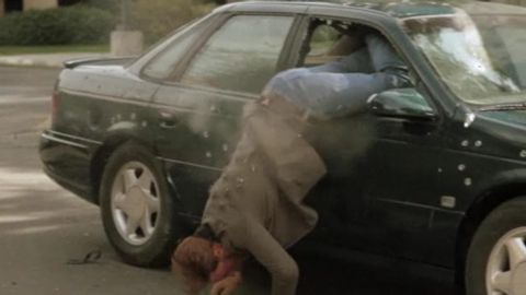 1993 Ford Taurus - Person falling out of a 1993 Ford Taurus, with bullet holes visible on the door and windshield.