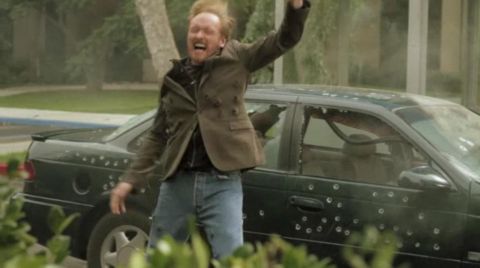 1993 Ford Taurus - A man reacts in front of a dark green sedan riddled with bullet holes.