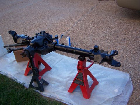 1992 Ford Bronco - A vehicle axle assembly is supported by jack stands on a driveway, possibly undergoing maintenance or painting.
