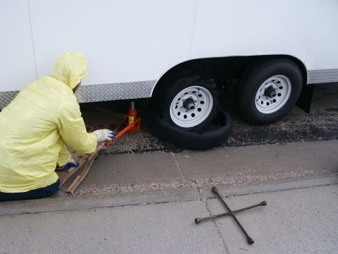 1990 Ford Bronco - A person is using a jack to lift a trailer while changing a flat tire.
