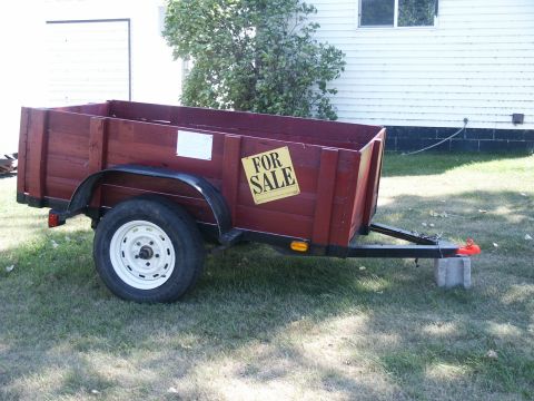 1990 Ford Bronco - A red wooden trailer is parked on a grassy lawn in front of a white building.