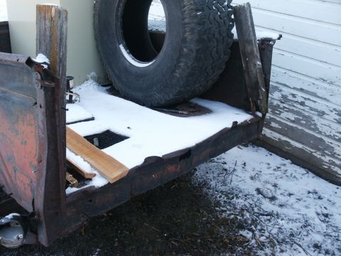 1990 Ford Bronco - Spare tire mounted on a rusty trailer bed covered in snow.