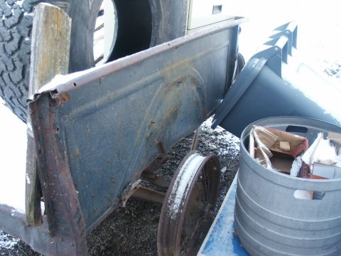 1990 Ford Bronco - An old truck bed sits outdoors with a large tire and a metal barrel nearby.