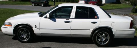 2005 Mercury Grand Marquis - This white sedan, believed to be a 2005 Mercury Grand Marquis, is shown from the side with custom wheels and a hood scoop.