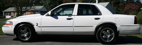 2005 Mercury Grand Marquis - Side profile of a white sedan with aftermarket chrome wheels.
