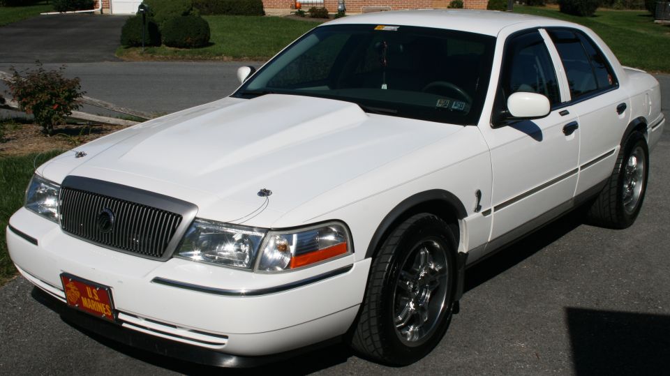White sedan with a scoop on the hood and chrome wheels. Has a US Marines plate on the front
