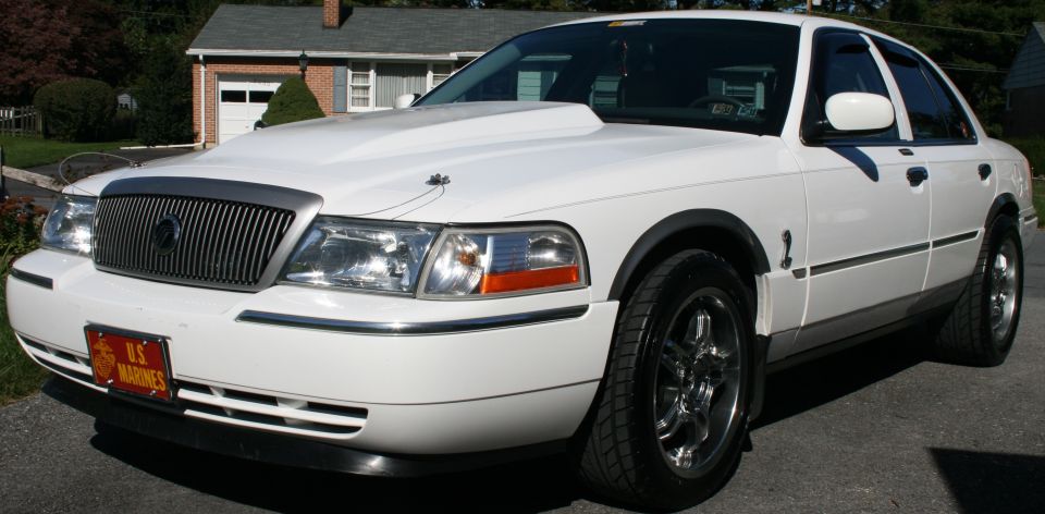 White sedan with a large hood scoop, chrome grille, and "U.S. Marines" license plate