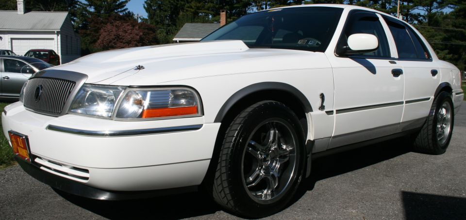 White sedan with aftermarket hood scoop and chrome wheels, front quarter view