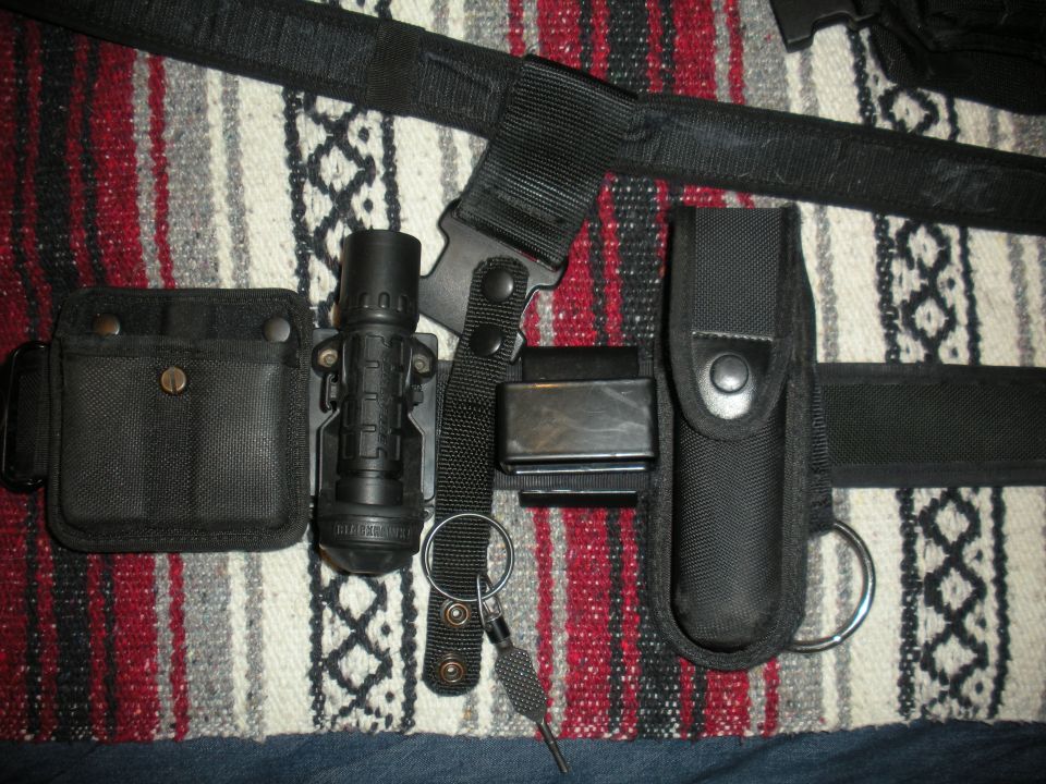 Utility belt with flashlight, magazine pouch, and other accessories laid out on a blanket