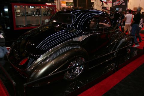 1998 Ford Crown Victoria - glossy black custom streamlined coupe hot rod with sweeping bodywork and chrome wheels displayed on a stand at an indoor show.