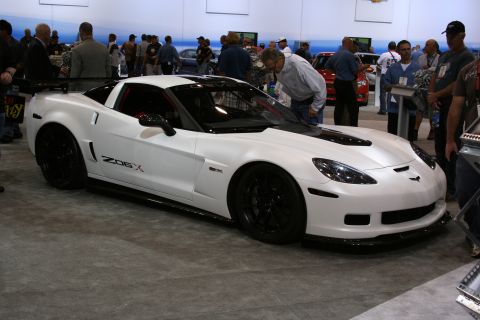 1998 Ford Crown Victoria - white Chevrolet Corvette Z06X coupe with black wheels and Z06X graphics displayed among crowds on an indoor show floor.