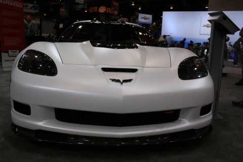 1998 Ford Crown Victoria - Front view of a matte white Chevrolet Corvette coupe with blacked-out headlights on display at an indoor automotive show.