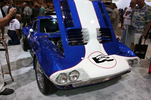 1998 Ford Crown Victoria - blue and white vintage-style Corvette Grand Sport coupe with its rear clamshell raised, number 6 on the nose, at an indoor show.