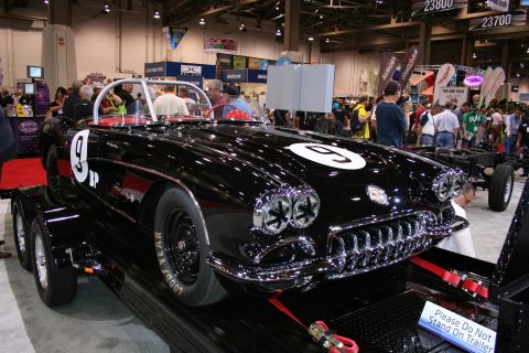 1998 Ford Crown Victoria - black early Chevrolet Corvette race car marked number 9 sits on a trailer at an indoor show beside a bare car chassis.