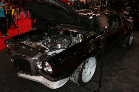 1998 Ford Crown Victoria - front three-quarter view of a black custom car shows a carbon-fiber nose, open hood and exposed engine on the show floor.