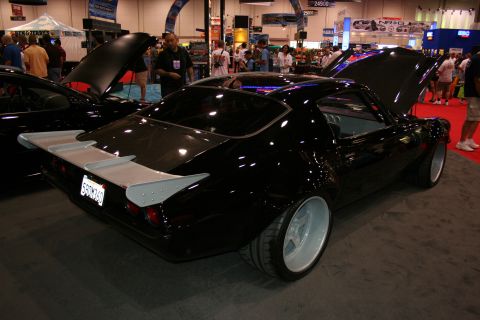 1998 Ford Crown Victoria - black custom fastback with a large rear wing and silver wheels is photographed from the rear three-quarter angle on a busy show floor.