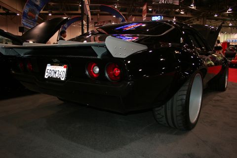 1998 Ford Crown Victoria - rear of a black custom car shows round taillights, a silver rear wing and a California plate reading 5BOM360 at an indoor show.