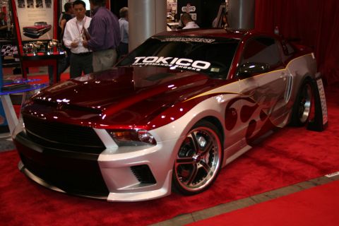 1998 Ford Crown Victoria - two-tone red and silver custom muscle coupe with flame graphics and a TOKICO windshield banner sits on red carpet at an indoor show.
