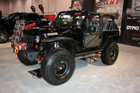 1998 Ford Crown Victoria - black lifted two-door Jeep Wrangler fitted with a front winch, snorkel and beadlock off-road wheels is displayed at an indoor automotive sh…