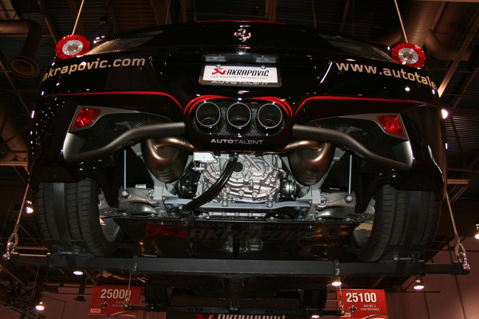 Underside rear view of black Ferrari on lift showing exhaust and engine