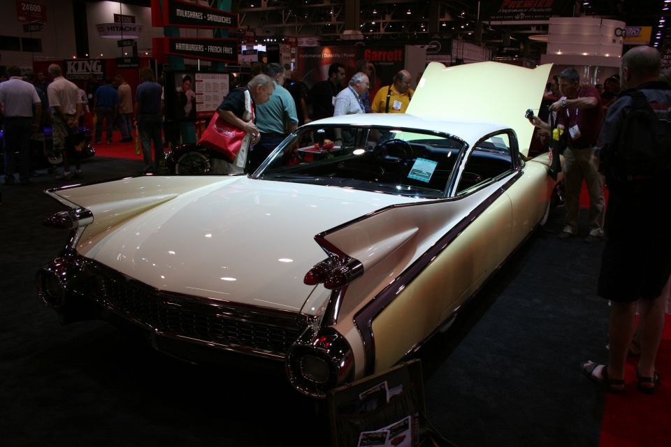 Cream 1950s Cadillac with tailfins and open hood at indoor car show