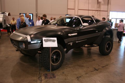 1998 Ford Crown Victoria - matte-black off-road sports vehicle with raised suspension, knobby tires and black wheels displayed indoors with a spec placard in front.