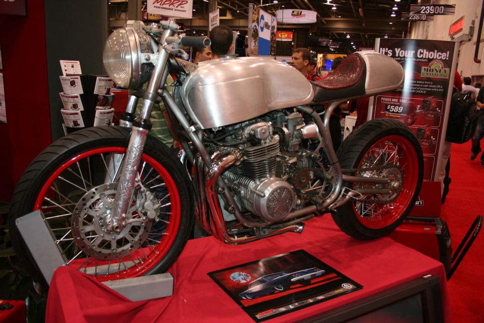 Bare-metal cafe racer motorcycle with red wheels on a show stand