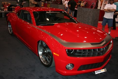 1998 Ford Crown Victoria - red fifth-generation Chevrolet Camaro with a matte hood stripe and large polished wheels on display at an indoor show.