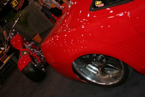 1998 Ford Crown Victoria - Close-up of the front fender, polished five-spoke wheel and chrome detailing of a glossy red sports car at an indoor booth.