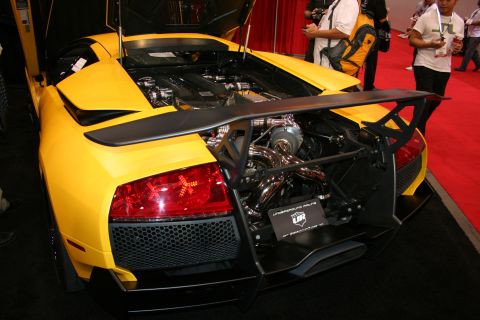 1998 Ford Crown Victoria - Rear view of a yellow Lamborghini Murcielago with an exposed V12 engine, chrome exhaust headers and a large carbon wing on a show stand.