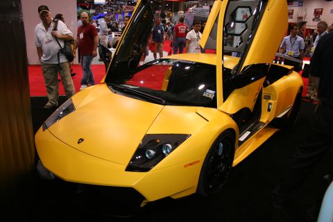 1998 Ford Crown Victoria - yellow Lamborghini-style supercar displayed with both scissor doors raised among crowds on a red show-floor carpet.