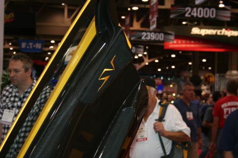 1998 Ford Crown Victoria - Detail of a raised black carbon-fiber supercar door bearing a yellow lightning-style SV emblem on a busy trade-show floor.