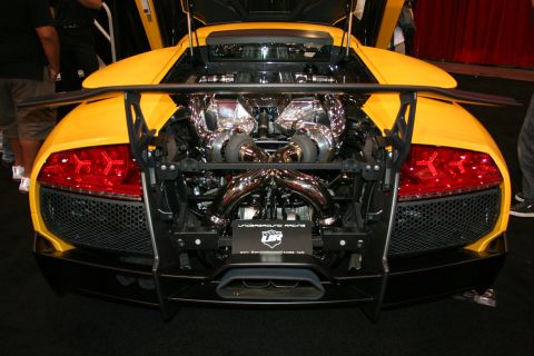 1998 Ford Crown Victoria - rear of a yellow supercar showing an exposed chrome twin-turbo engine, tube framework, red taillights and dual exhaust.