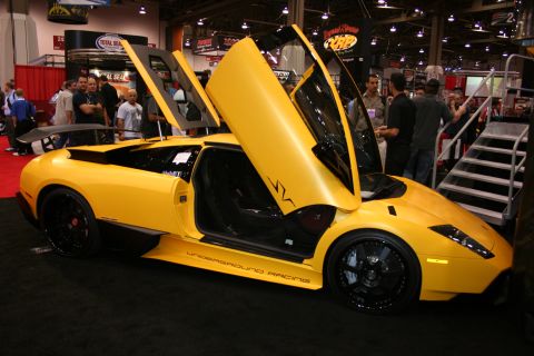 1998 Ford Crown Victoria - yellow supercar with scissor doors raised and 'Underground Racing' side graphics parked beside a display ramp at a trade show.