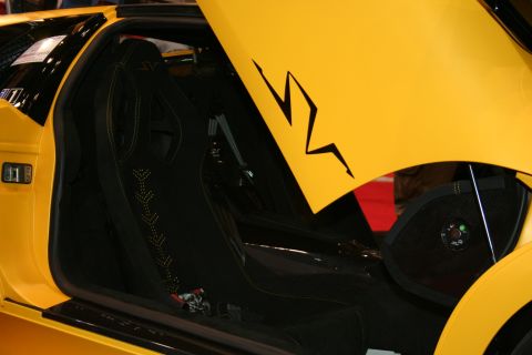 1998 Ford Crown Victoria - Interior detail of a yellow supercar showing a black carbon racing bucket seat through the open door beside an SV lightning graphic.
