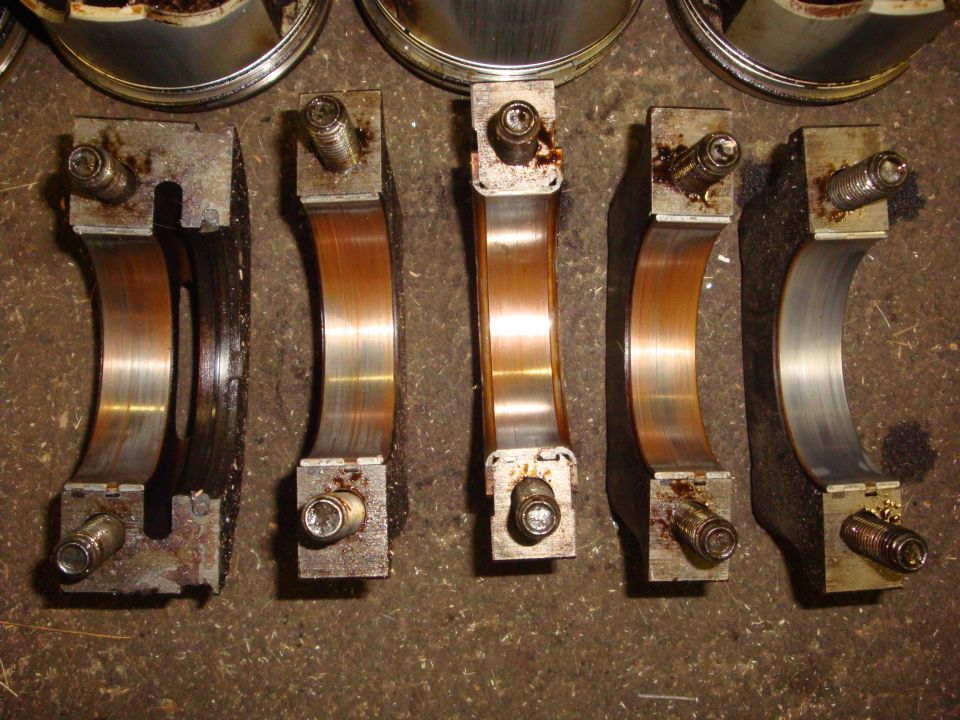 Engine crankshaft bearings with bolts attached, laid out on a rough surface