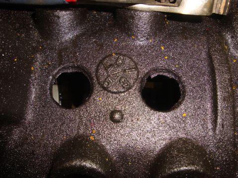 1989 Ford Bronco - Close-up of an engine block casting with a stamped circular marking and two holes.