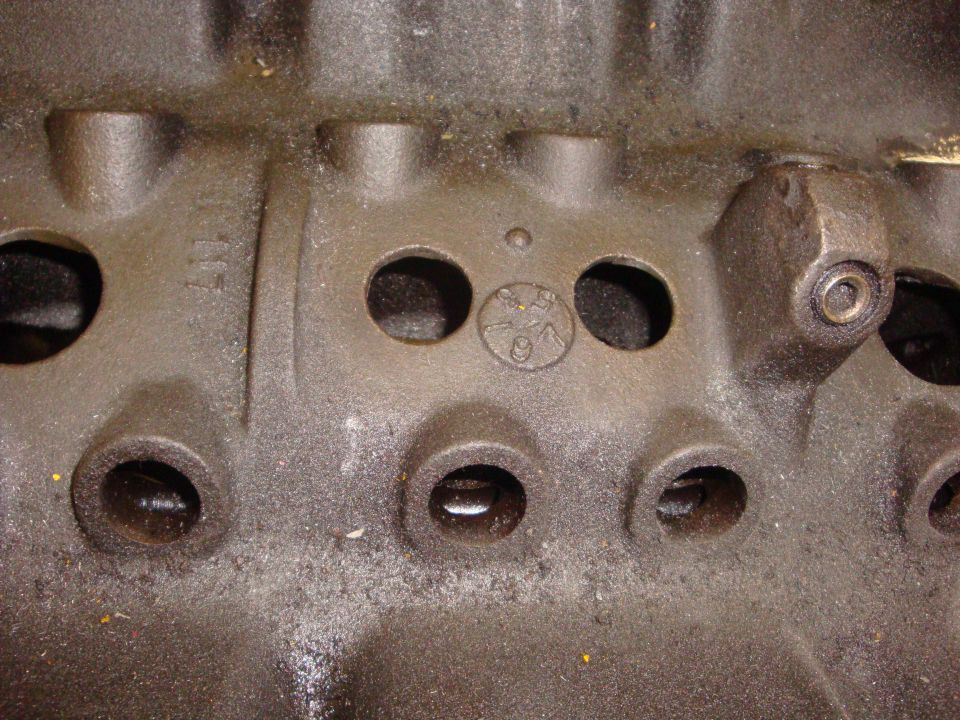 Close-up of bare cast-iron cylinder head showing pushrod holes and casting mark