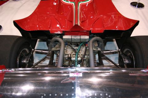 1998 Ford Crown Victoria - Low rear view beneath a red Formula 1 car revealing curved exhaust headers, suspension and chassis above a polished panel.