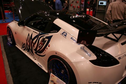1998 Ford Crown Victoria - white modified sports coupe with black tribal side graphics, open hood, blue-spoke wheels and a tall rear wing at a show.