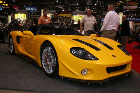 1998 Ford Crown Victoria - Front three-quarter view of a yellow mid-engine sports car with round headlights and silver wheels surrounded by show attendees.