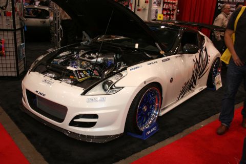 1998 Ford Crown Victoria - white modified sports coupe with black tribal graphics, blue wheels and an exposed turbocharged engine under its raised hood.