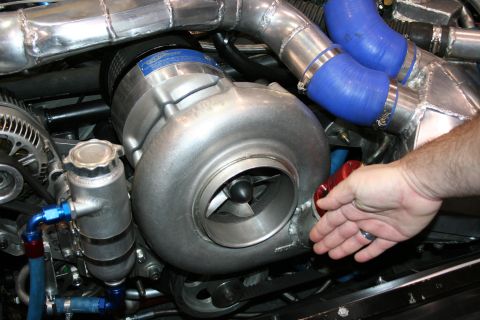 1998 Ford Crown Victoria - Close-up of a large turbocharger compressor housing with an alternator, polished pipes and blue hoses, a hand resting on the engine.