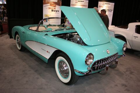 1998 Ford Crown Victoria - turquoise and white 1950s Chevrolet Corvette convertible with whitewall tires and its hood raised on a display floor.