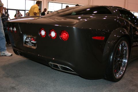 1998 Ford Crown Victoria - Rear view of a black custom Corvette-style coupe with quad round taillights, dual exhaust and chrome wheels at a show.