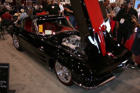 1998 Ford Crown Victoria - black classic Corvette coupe with red interior and raised hood revealing a chrome engine, displayed on a carpeted show floor.
