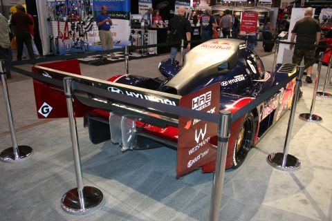 1998 Ford Crown Victoria - dark Red Bull and Hyundai-liveried prototype race car shown rear-on within a stanchioned booth at an indoor show.